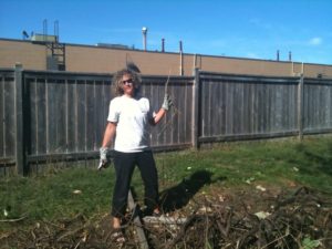 Kerry, about 5 feet tall with short, curly blond hair wearing a white T shirt and black pants, holding a huge set of snippers up in victory