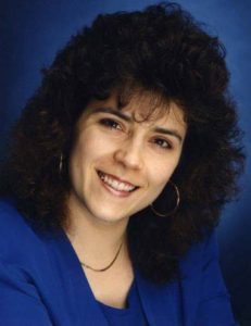 My headshot from the early 1990s. I have huge, curly hair, big hoop earrings and I'm posed in the classic head-tilt