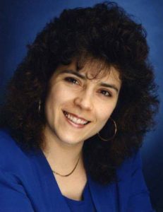 My headshot from the early 1990s. I have huge, curly hair, big hoop earrings and I'm posed in the classic head-tilt 