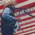 Hank Williams Jr singing on stage in front of a backdrop of an American flag