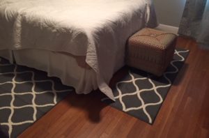 End of the bed shows a rug at the end and one at one side - both are grey with white lattice patterns