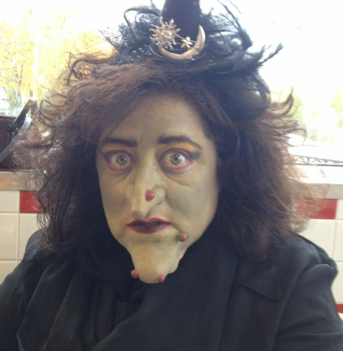Closeup of a witch - long frizzy black hair, giant chin, green skin and a huge wart on her nose