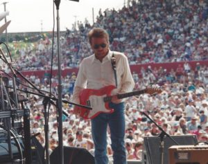 A shot of Parnell playing his guitar from the perspective of backstage. A massive audience can be seen behind him.