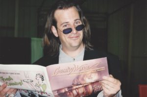 Robert Reynolds pretending to read an issue of Country Wave Magazine