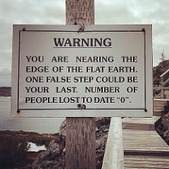 Sign reads: WARNING! You are nearing the edge of the flat earth. One false step could be your last. Number of people lost to date: 0.