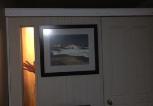 booth has a long, slim window on the left side, a print of Peggy's Cove and a closed door. White trim finishes the top and you can see Derek's hand waving in the window