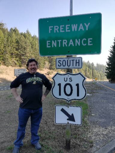 Derek stands beside an entrance sign for Highway 101 south