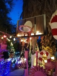 a toilet seat on a backstop as a basketball net with lights and giant candy canes in the background