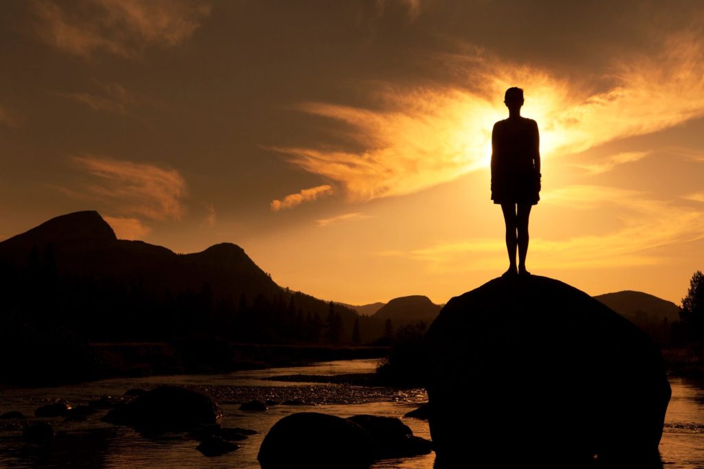 silhouette of a person standing on a rock with the sunset in front of them