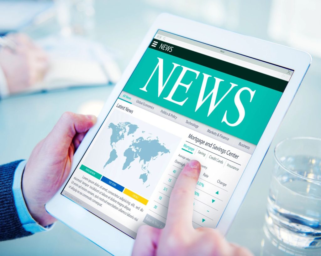 a man's hands holding a tablet with the headline "news" showing on it