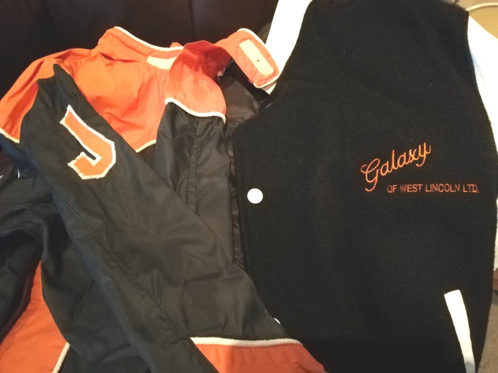 Dad's riding jumpsuit is black with an orange collar and orange J. His Galaxy of West Lincoln jacket is a black wool bomber-style with orange lettering