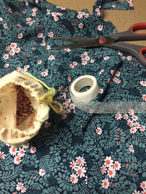 green material with white flowers, scissors, an open bag of cedar chips and hemming tape. 