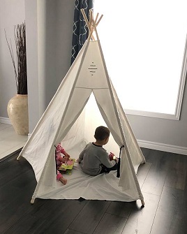 Ryker and Vienna in a white teepee about six feet tall, both reading books. The teepee is set up on a dark laminate floor in their living room