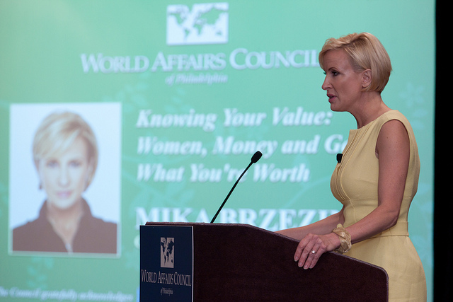 Mika Brzezinski wearing a yellow, sleeveless dress at a podium speaking to the World Affairs Council