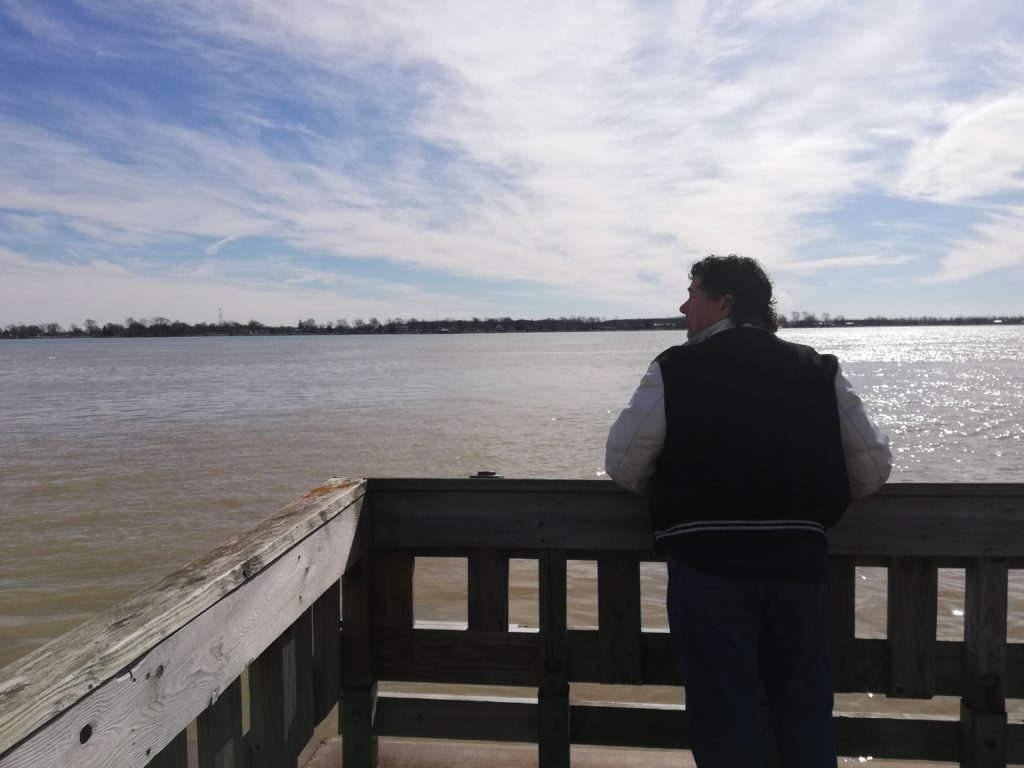 Derek leaning over a railing looking out at the water with a beautiful blue sky ahead of him