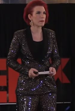 screen capture of sociologist Maja Jovanovic. Tall woman with bright red hair wearing a sequinned silver suit and black top.