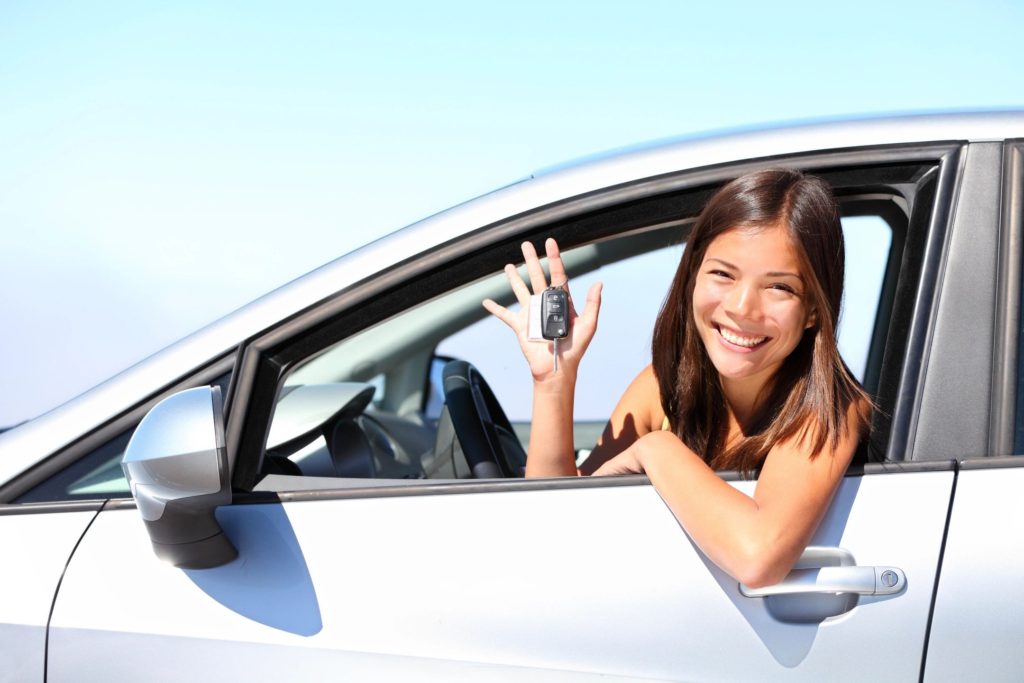 Young woman sitting in driver's seat of a car, proudly holding up keys