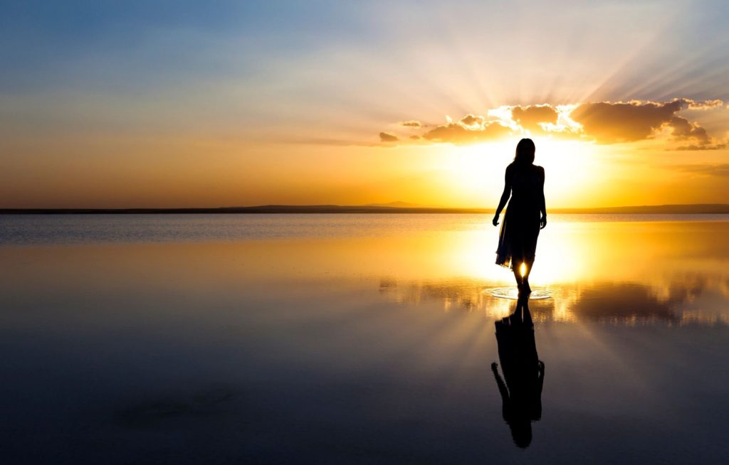 woman in silhouette walking on a beach toward the sunset