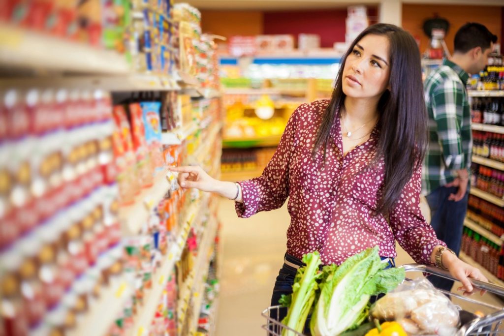 woman selecting a can from a packed grocery store shelf