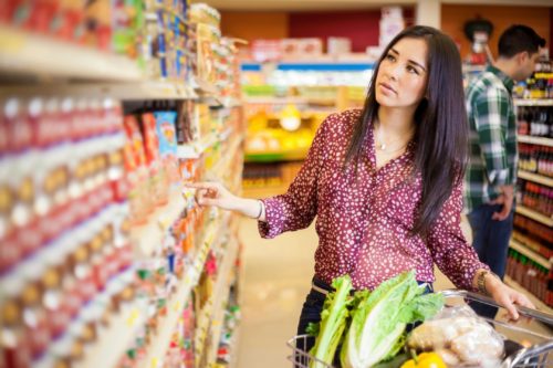 woman selecting a can from a packed grocery store shelf