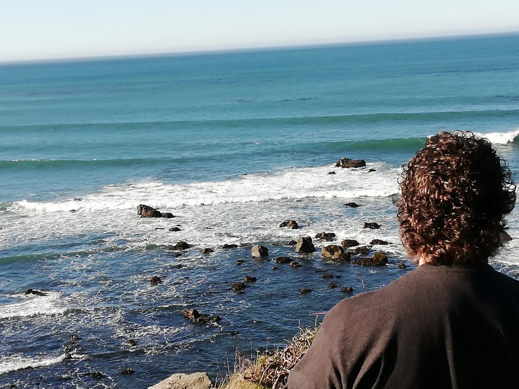 The back of Derek's head in the foreground with mid-size waves crashing into rocks along the Oregon coast in the background