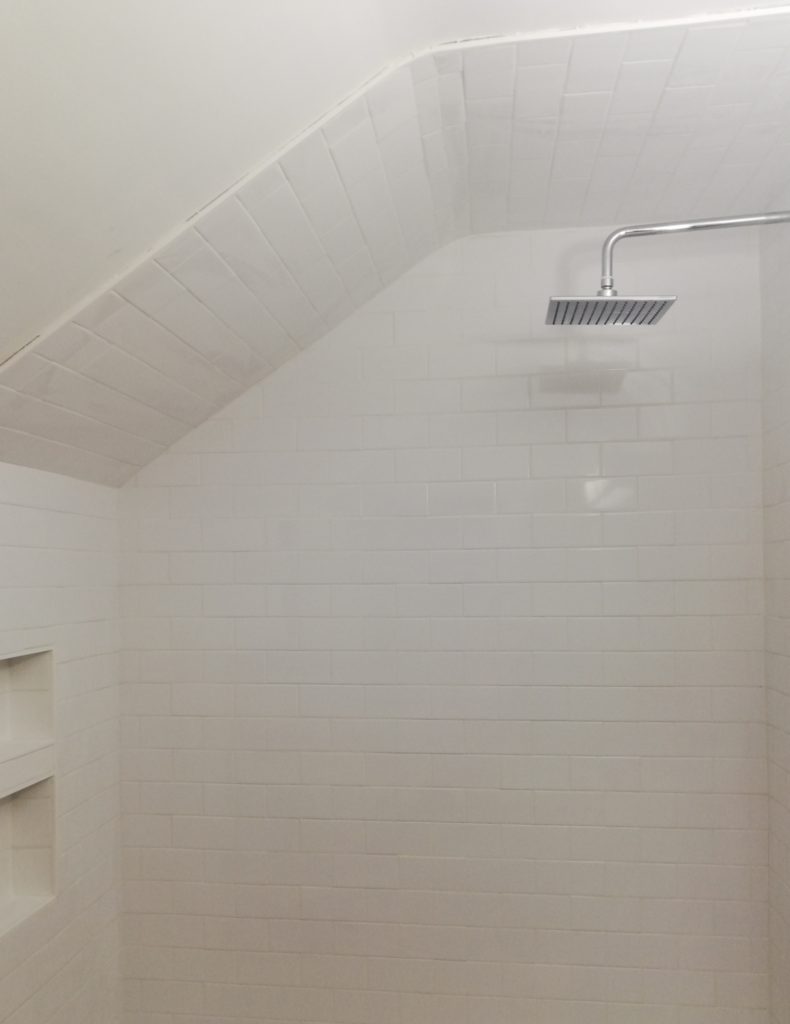 shower is tiled with white subway tiles and grouted white, with a cubby with two shelves at the back, also tiled
