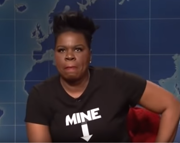 SNL cast member Leslie Jones looking into the camera, wearing a black T shirt with the word MINE in white and an arrow pointing down.