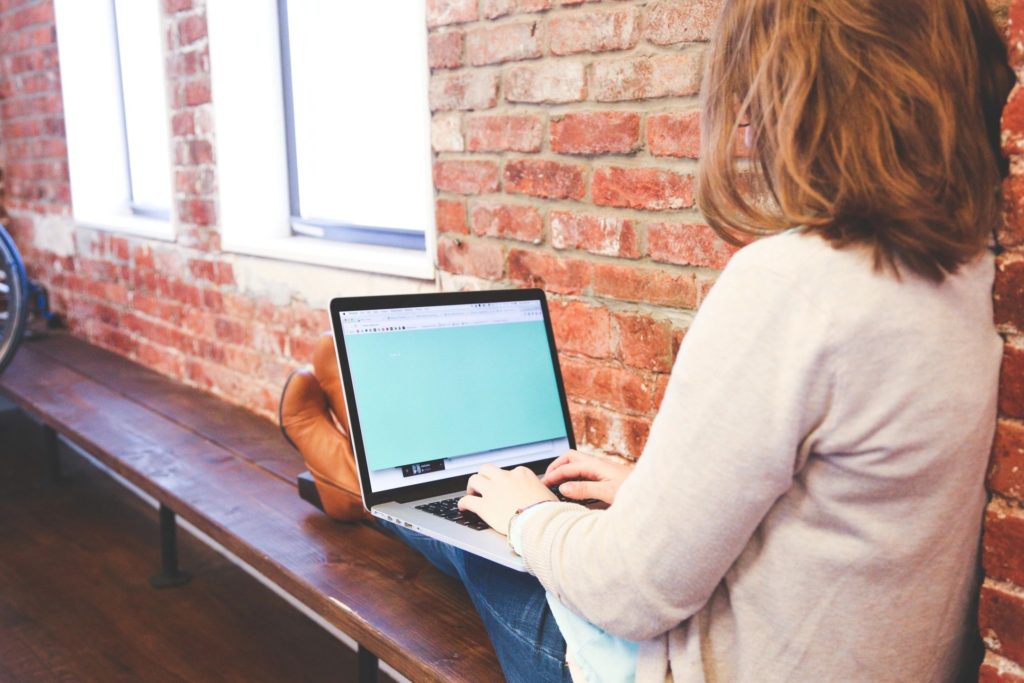 woman sitting on a ledge in a Starbucks-like coffee shop working on a laptop on her lap