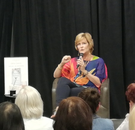 Erin holding a microphone, seated, talking to an audience about her book