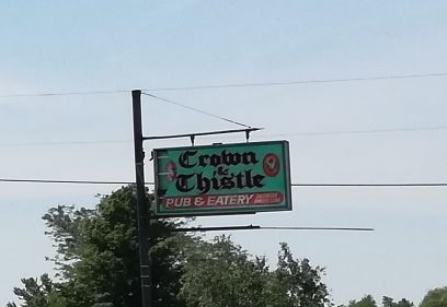 Old sign, green, white and red, reads Crown and Thistle Eatery and Pub