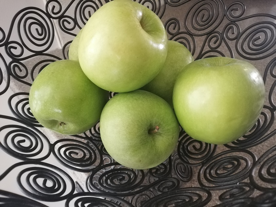 A black bowl made up of wire swirls holding a half dozen green Granny Smith apples