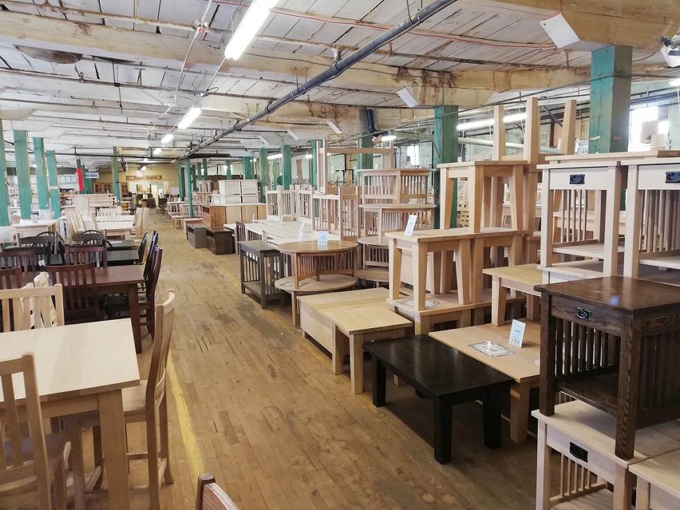 Dining tables, coffee tables, chairs and other types of tables piled and stretching down a long room with wood plank flooring.