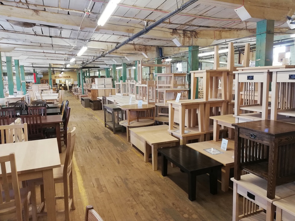 Dining tables, coffee tables, chairs and other types of tables piled and stretching down a long room with wood plank flooring. 