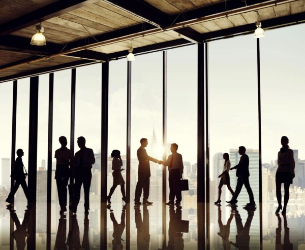 Outlines of eight people chatting or shaking hands against a wall of glass windows.