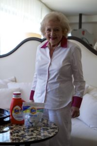 Betty White in a white outfit with red collar and cuffs.