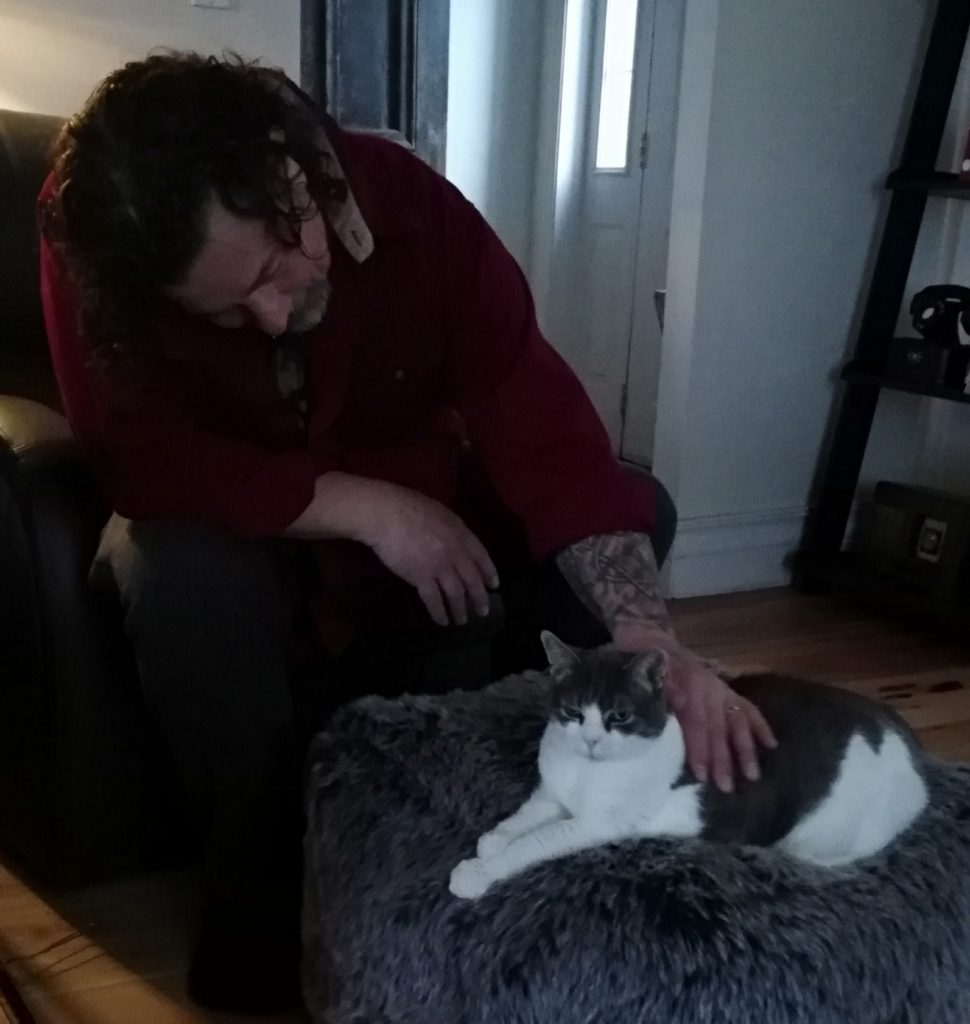 Derek petting a happy cat as she sits on her fuzzy pouf.