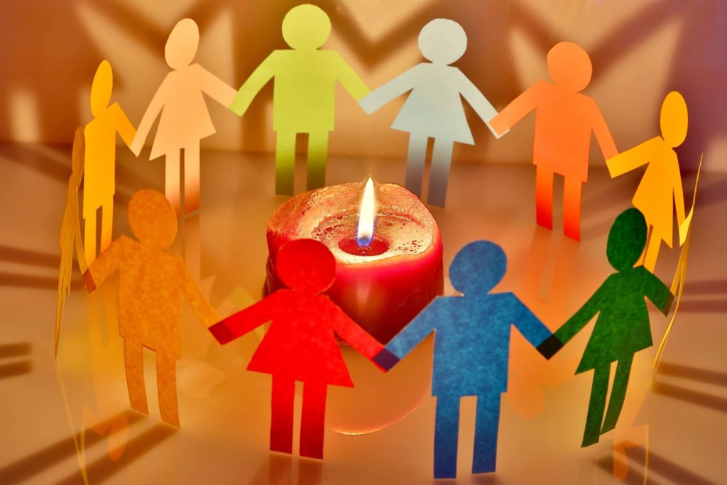 Little human figures cut out of different colour paper, joined in a circle around a candle