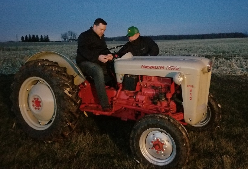 Colin sits on the tractor and looks seriously at the steering column as Rob, standing beside the beast, shows him how it works. 