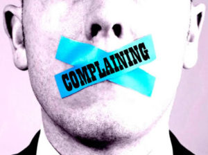 A man's face with blue tape across the mouth and the word COMPLAINING