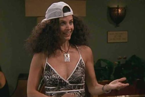 Courteney Cox as Monica Geller on Friends with huge, frizzy hair and wearing a white ball cap.