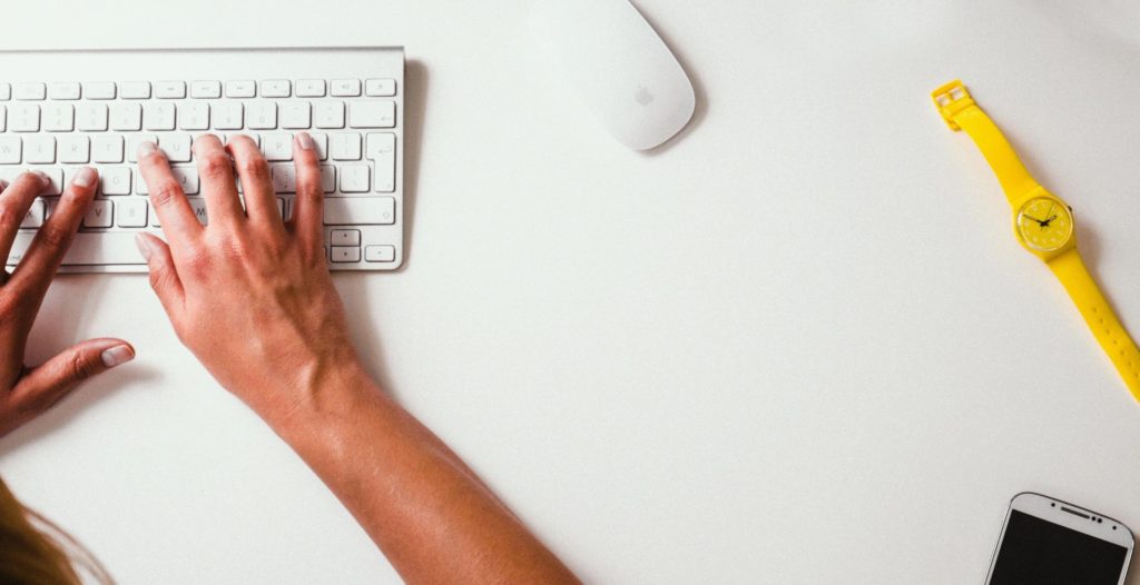 Hand on a laptop keyboard with a mouse and a yellow watch in view