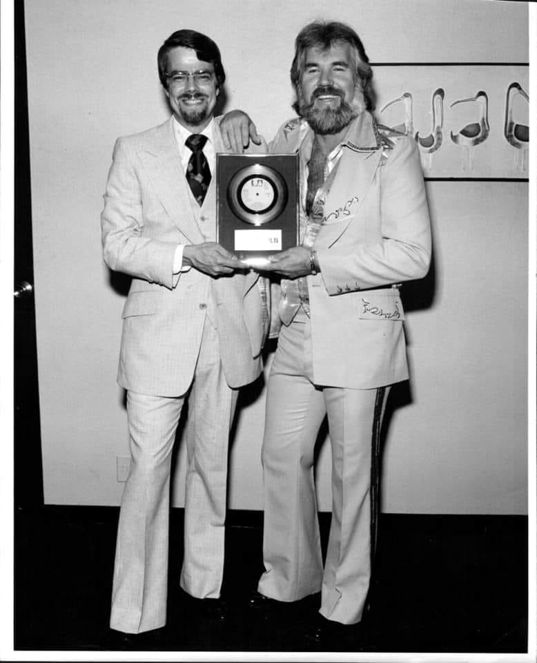 Nevin Grant and Kenny Rogers in a black and white photo, both wearing suits and holding a gold record