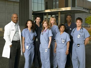 The main cast of Grey's Anatomy posing in their hospital scrubs and white lab coats