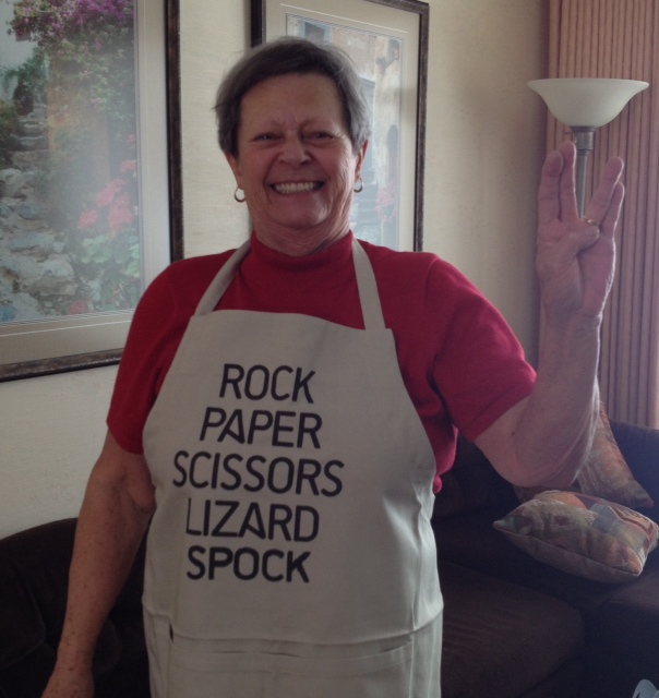 My Mom wearing a Big Bang Theory apron that reads Rock Paper Scissors Lizard Spock, and making the Live-long-and-prosper hand signal from Star Trek