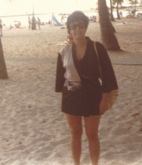 Mom on a beach, thin, in a bathing suit cover-up with huge sunglasses and a towel over her shoulder. 