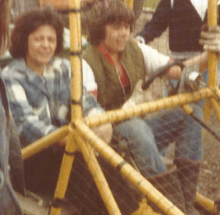 A bit blurry. An image of Mom and my brother Kevin behind the wire of a dune buggy as they prepare for a ride. Kevin is at the wheel.