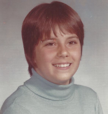 Me, smiling in a school picture, with short hair and uneven bangs. 