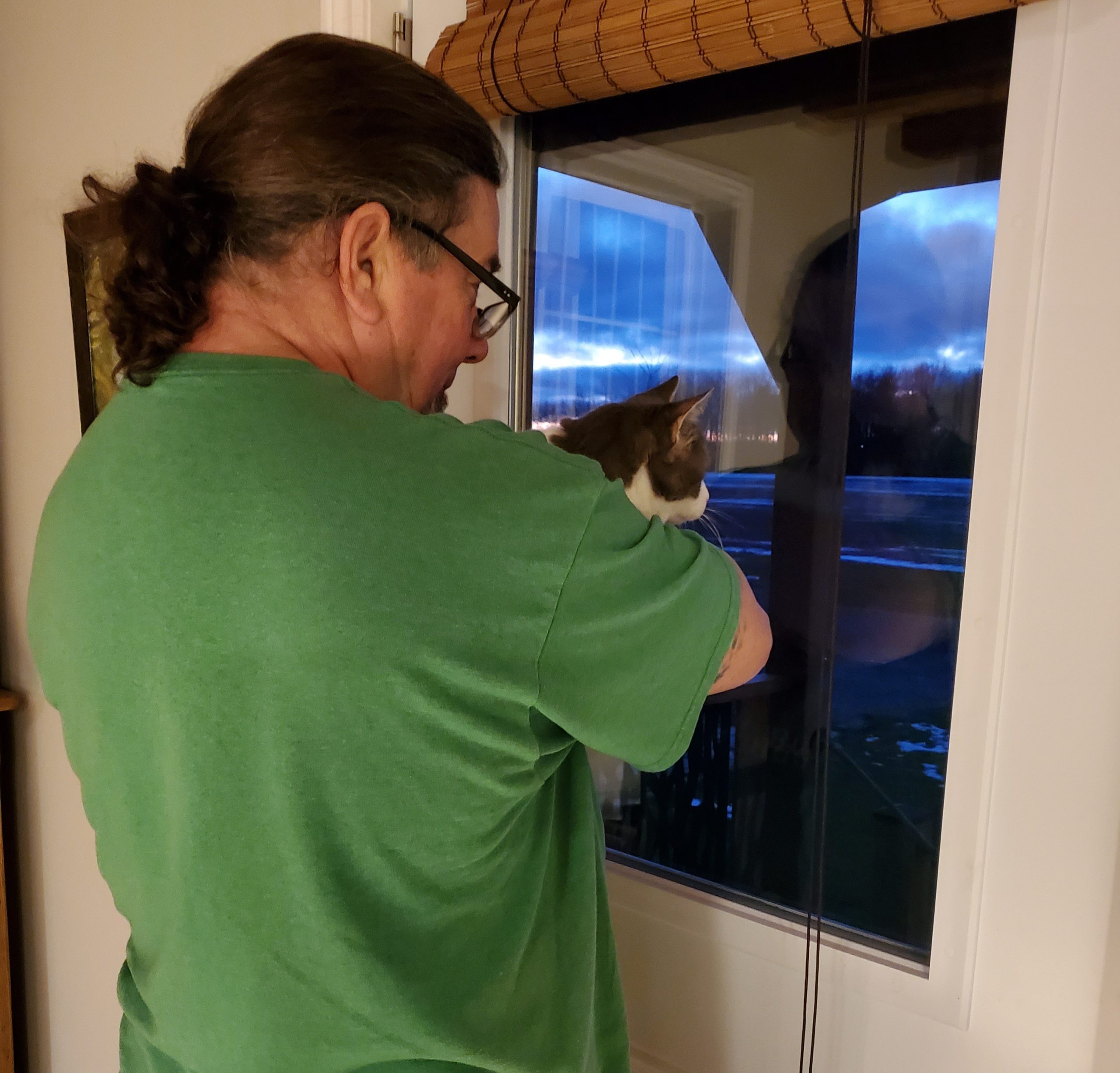 Derek holding Sugar up to a window and they're both looking outside into the night