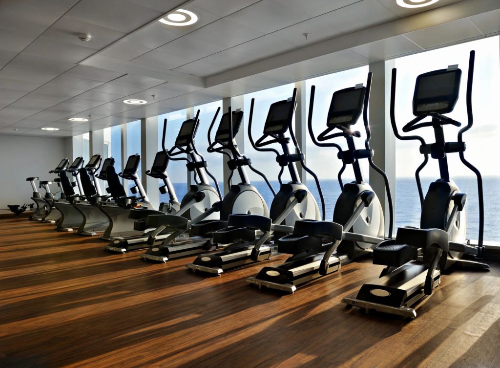 A row of treadmills on a hardwood floor in front of floor to ceiling windows