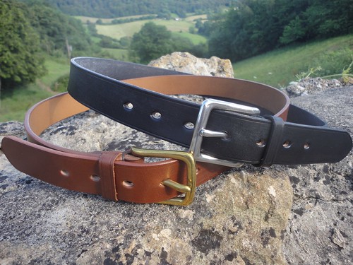 a brown and a black leather belt sitting on a rock